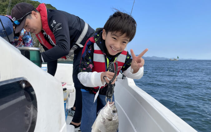 子供が船上で釣った魚を持って笑顔でピースをしている写真